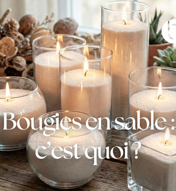 Bougies en sable allumées dans des contenants en verre de différentes formes, posées sur une table en bois, créant une ambiance chaleureuse et naturelle.